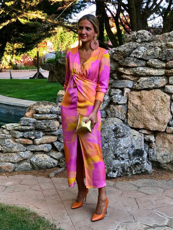 a super bold garden wedding guest look with a watercolor midi dress in orange, pink and yellow, orange shoes and a gold mini clutch