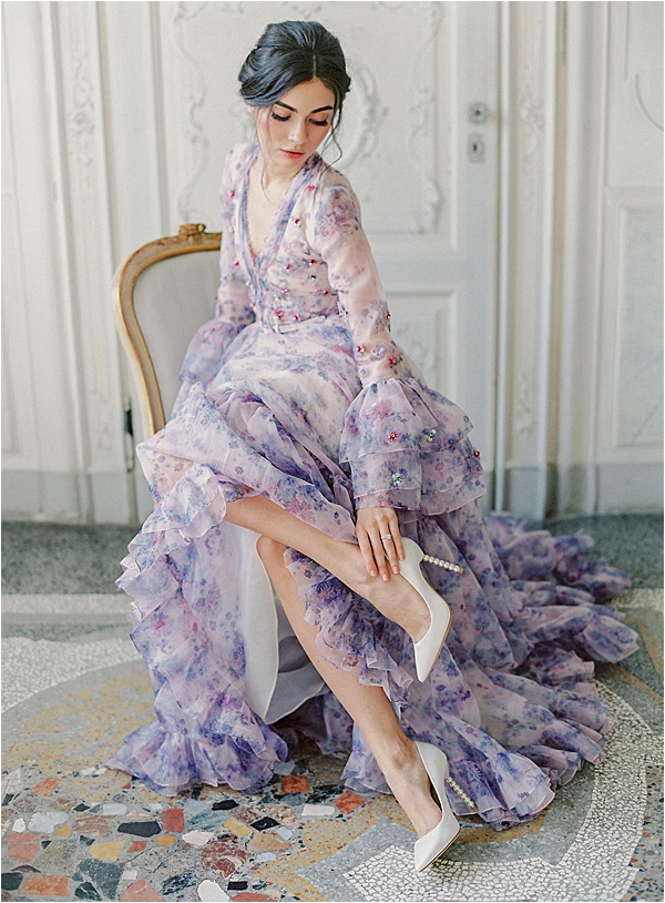 a lilac A-line wedding dress with bell ruffle sleeves, a V-neckline, a ruffle skirt and white shoes with pearl heels