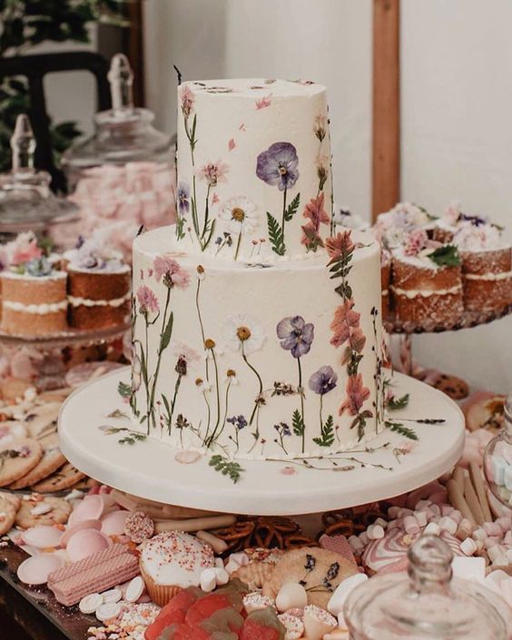 a very delicate white buttercream wedding cake with pressed white and pastel flowers and leaves is a great idea for spring