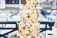 43 a white buttercream wedding cake with lots of pressed colorful blooms and herbs and some faux butterflies for a beautiful summer wedding