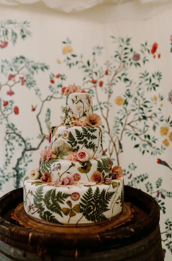 a white buttercream wedding cake with pressed dried blooms and leaves and some pastel flowers on top for a garden wedding