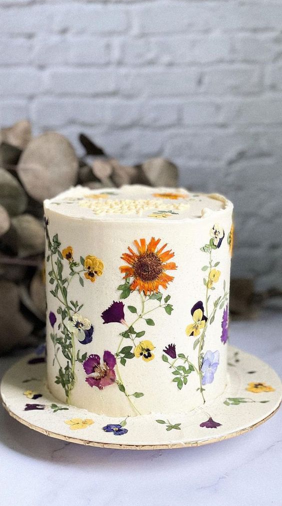 a white buttercream wedding cake with uneven edge and bright pressed flowers and leaves is a gorgeous idea for a spring or summer wedding