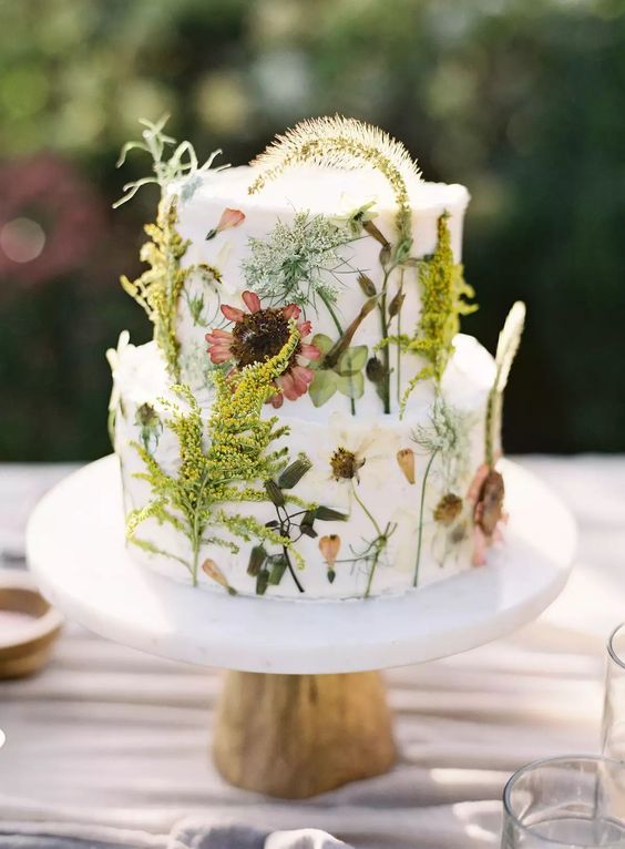 an awesome white buttercream wedding cake with pressed dried blooms and herbs is a gorgeous idea for a boho wedding