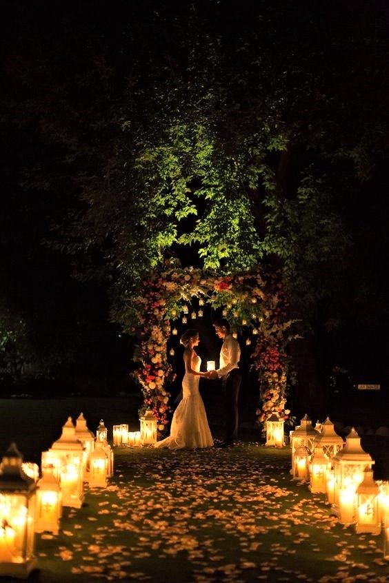 a cozy and charming evening wedding ceremony with lots of candle lanterns and with a bold floral wedding arch