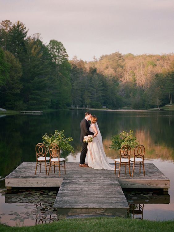 a fantastic outdoor wedding ceremony space with a lake view, greenery arrangements and elegant chairs for a small wedding