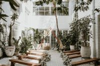 a small and intimate backyard with lots of potted plants, a triangle wedding arch with greenery and white blooms, white florals lining up the aisle