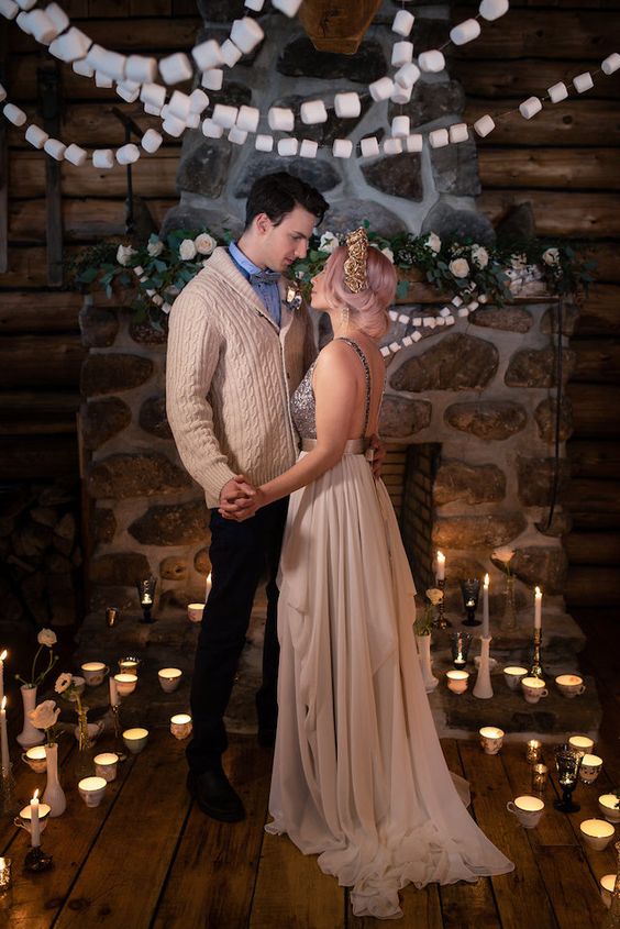 a beautiful chalet wedding ceremony space with a fireplace, marshmallow garlands, lots of candles and greenery and blooms around