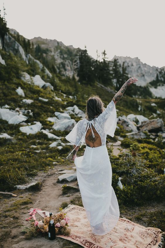 a boho mountain bride wearing a neutral wedding dress with lace appliques, a cutout back and wide sleeves is amazing