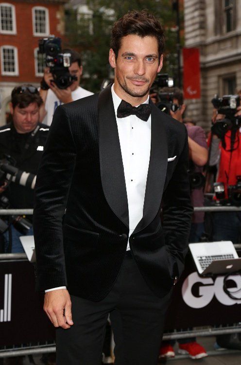 David Gandy wearing black trousers, a white shirt with black buttons, a black corduroy dinner jacket with matte lapels and a printed bow tie
