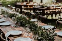 15 a beautiful and simple wedding reception space with a lush greenery runner, white linens, candles and gold-rimmed glasses