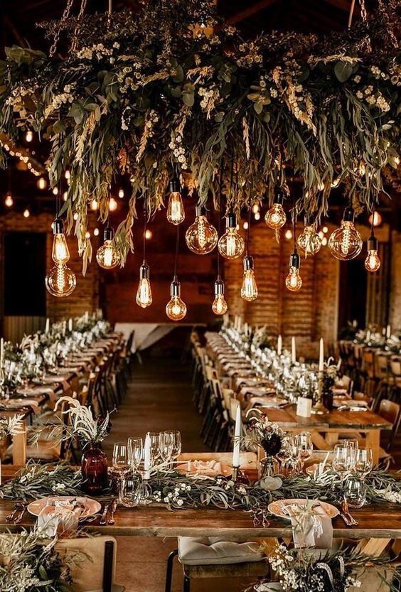 a beautiful chalet wedding reception space with a lush and textural greenery chandelier with bulbs, greenery runners and centerpieces and tall candles