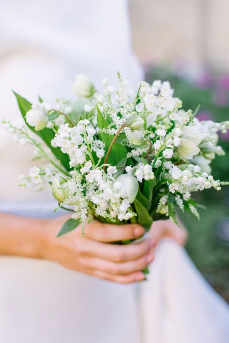 an all-white wedding bouquet of lily of the valley, snowdrops, greenery, tulips is a beautiful idea for a spring bride