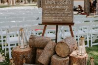 21 a cozy and lovely wedding ceremony space with white chairs, petals on the ground, tree stumps, candle lanterns and a sign