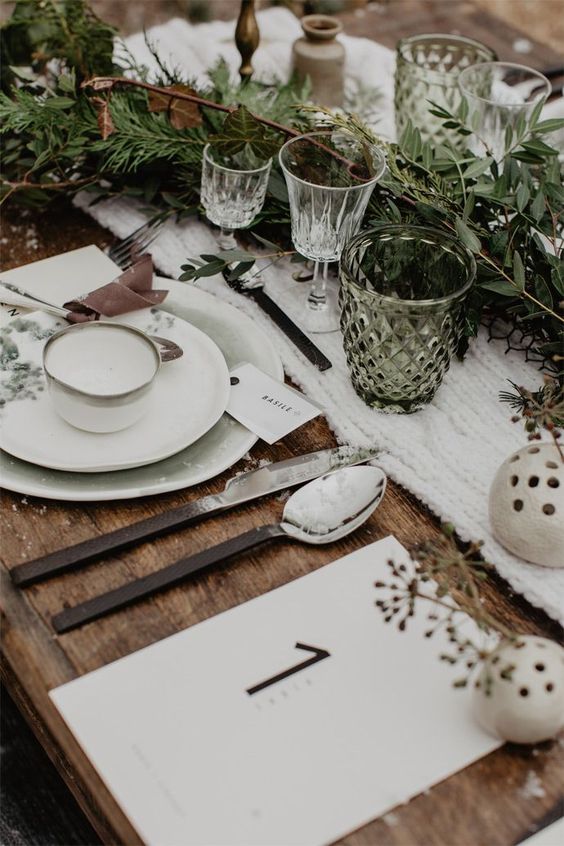 a hygge wedding table setting with a white knit table runner, simple porcelain, an evergreen table runner and berries