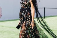26 a fantastic black midi dress with colorful floral embroidery, a high neckline, capelet-like sleeves and a semi sheer skirt, black shoes and a clutch