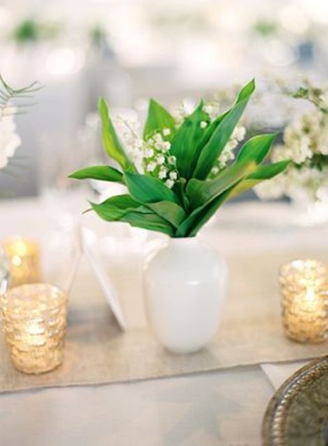 a delicate and stylish wedding centerpiece of a white vase and lily of the valley is a good idea for a spring wedding and you can DIY