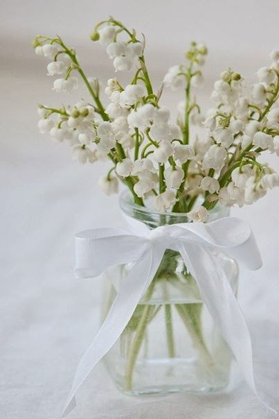 a delicate spring wedding centerpiece of a clear vase with a ribbon bow and lily of the valley is a lovely idea for both spring or summer