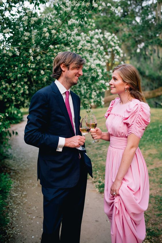 a feminine pink maxi dress with a square neckline, draped puff sleeves, a pleated skirt and elegant earrings for a black tie wedding