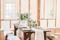 30 a simple and cozy chalet wedding reception space with neutral linens, greenery, tall and thin candles and benches with faux fur