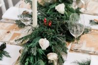 31 a simple and cozy winter chalet wedding tablescape with an uncovered table, an evergreen, berry and white rose table runner and tall candles