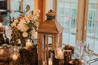 33 a wedding decoration of moss, tree stumps, candles, a large candle lantern and white blooms and greenery is perfect for a chalet wedding