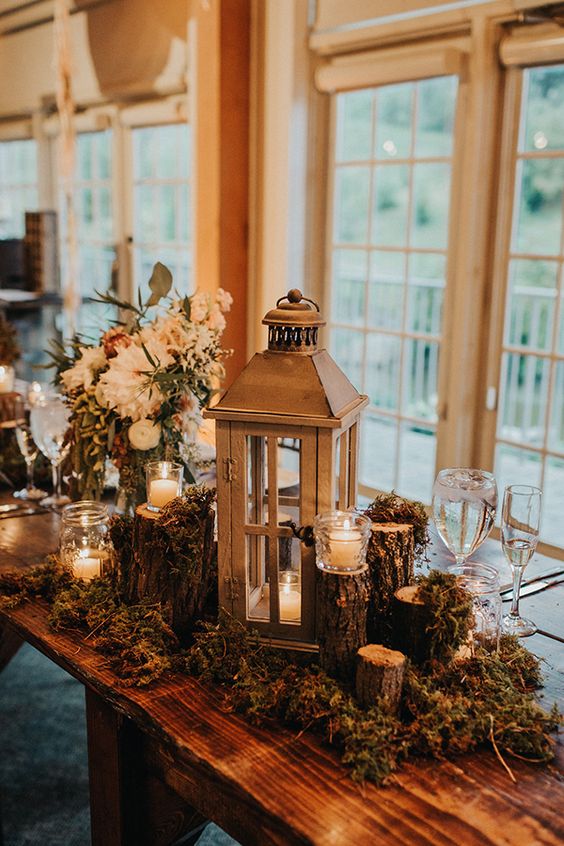 a wedding decoration of moss, tree stumps, candles, a large candle lantern and white blooms and greenery is perfect for a chalet wedding
