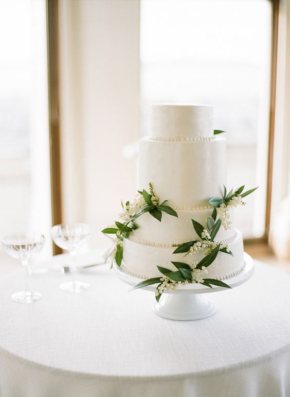 a white buttercream wedding cake decorated with lily of the valley and greenery is a very chic and beautiful idea for spring