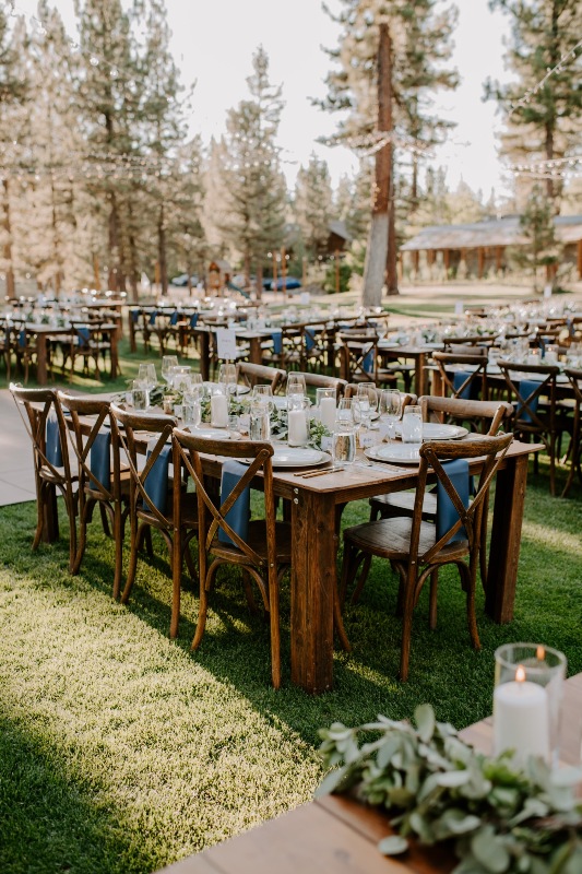 an outdoor chalet wedding reception space with stained furniture, stained chairs, navy napkins, greenery runners and pillar candles
