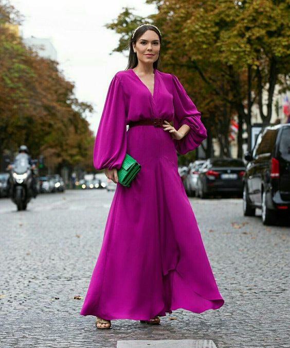 a purple high low maxi dress with puff sleeves and a deep neckline, a belt, an emerald clutch is amazing