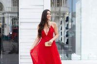 40 a red maxi dress with spaghetti straps, a depe neckline, a pleated skirt and nude shoes plus a neutral clutch