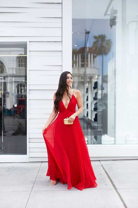 a red maxi dress with spaghetti straps, a depe neckline, a pleated skirt and nude shoes plus a neutral clutch