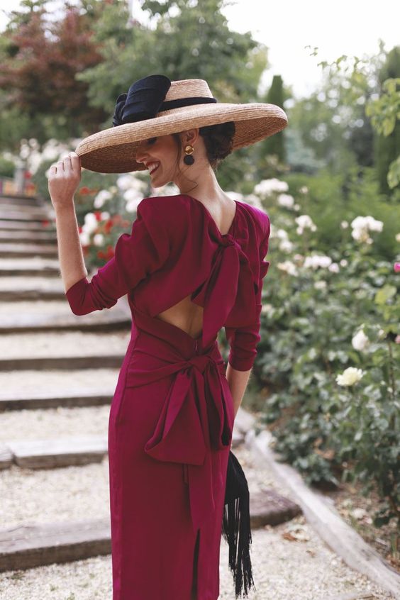a refined and beautiful fuchsia fitting midi dress with short sleeves, accented shoulders, a cutout back with a sash and a wide brim hat