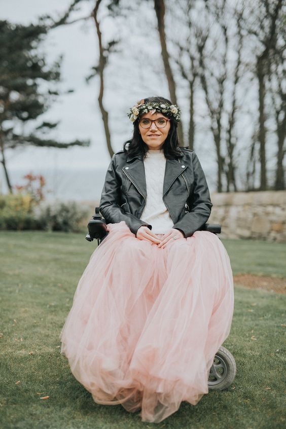 a chic bridal look with a white jumper, a pink tulle skirt, a black leather jacket, a floral crown and burgundy glasses