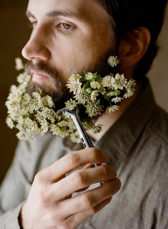 a groom rocking white blooms in his beard looks unusual and bold and such blooms will add a festive feel to the outfit