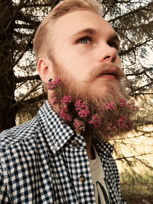 a groom wearing a romantic beard accented with mauve and purple blooms looks dreamy and these blooms add a touch of color to his look