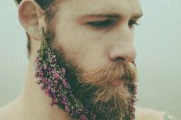 a hipster groom rocking a beard with pink and purple blooms attached to it looks unusual and very bold