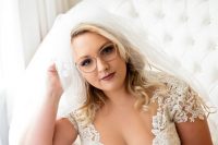 a lovely bridal look with a chic lace wedding dress with a covered deep neckline, short sleeves and eyeglasses in a blush frame