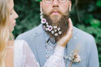 a pretty and unusual groom’s look with a serenity blue suit, a blue floral shirt and a beard with white blooms