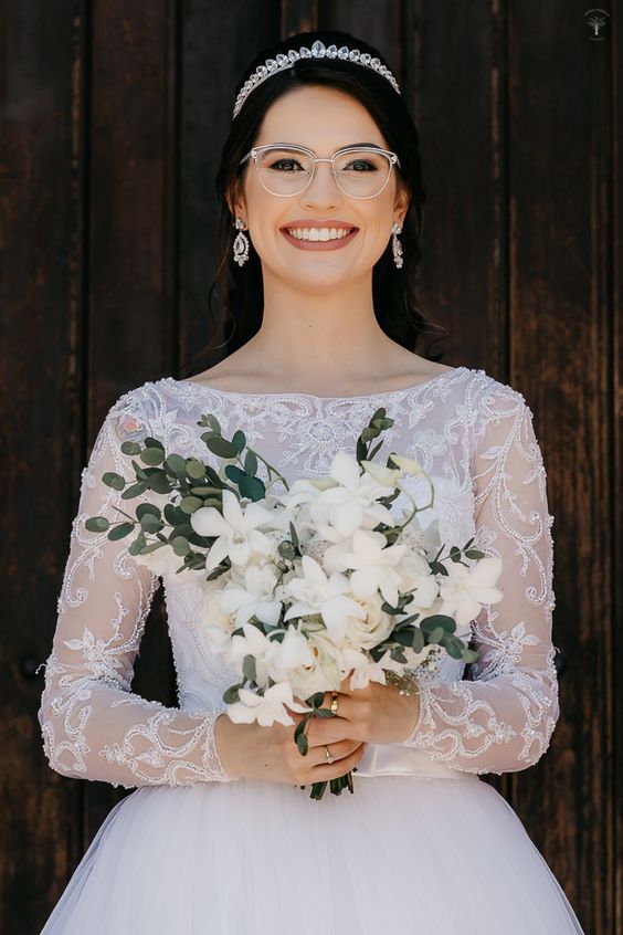 a refined bridal look with a lace wedding ballgown, statement earrings and a tiara plus clear and white framed eyeglasses