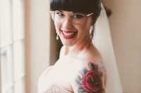 a romantic bridal look with a blush strapless wedding dress, bold bride’s tattoos shown off, delicate nude glasses and chic earrings