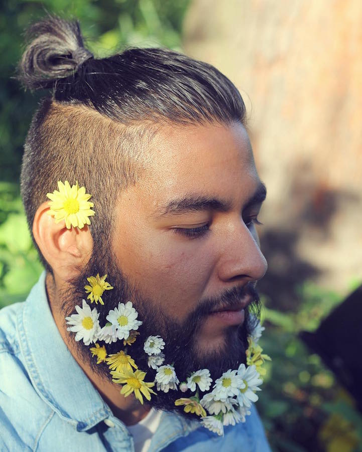 a trendy top knot and a delicate yet bright flower beard with white and yellow blooms compose a cool hipster look