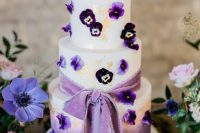 02 a beautiful ombre white to purple wedding cake decorated with gold leaf, with pansies and a purple ribbon bow is amazing