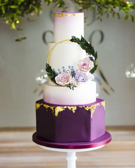 a bold and catchy wedding cake with ombre lilac, white and deep purple tiers, with gold leaf and pastel blooms and greenery