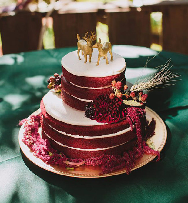 a boho fall red velvet wedding cake with glazing, with bold burgundy blooms, berries and wheat, with gold deer cake toppers is super cool