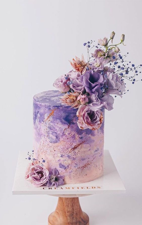 a breathtaking blush to purple watercolor wedding cake decorated with copper glitter, fresh lilac and pink blooms is a bold statement
