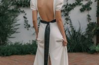 08 a fantastic white wedding dress with a square cutout back, puff sleeves, a slit on the back with buttons, a black sash, black flower earrings and a black bow accenting the hairstyle