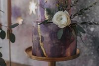 10 a dreamy celestial wedding cake done in the shades of purple and lilac, with gold glitter and foil, with a white bloom and greenery