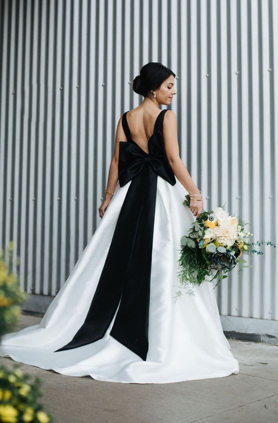 a modern wedding ballgown with black straps on the cutout back and an oversized black bow, with a train for an ultra-modern look
