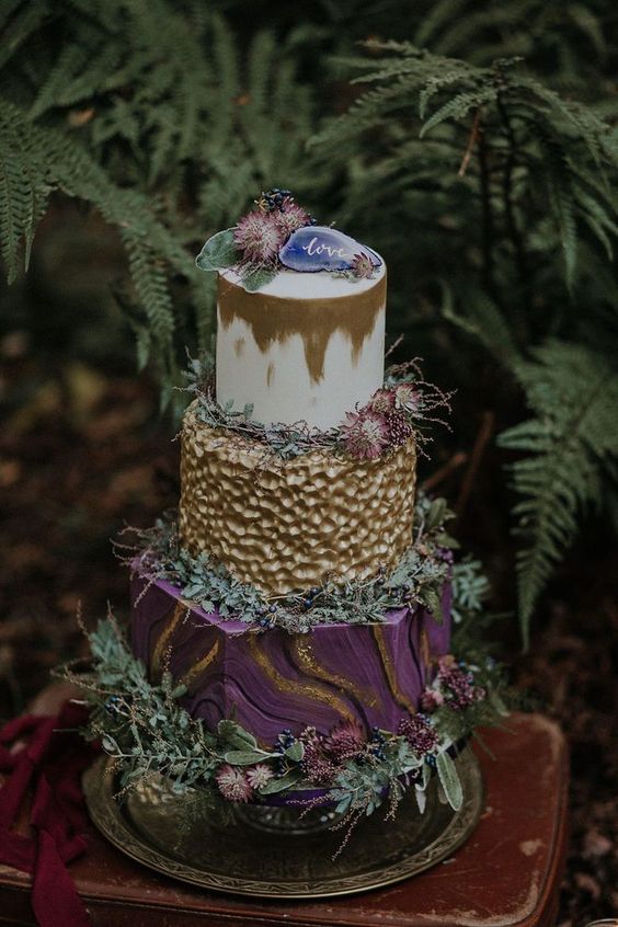 a gorgeous woodland boho wedding cake with a white and gold, a textural gold, purple and gold tier, dried purple blooms and greenery and an agate slice on top
