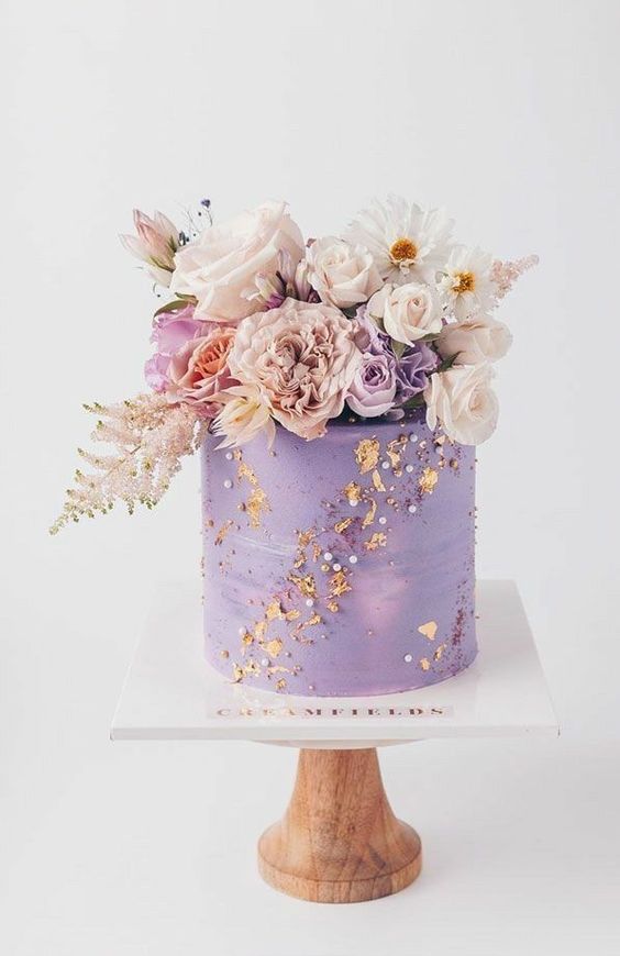 a jaw-dropping purple wedding cake decorated with dried flower petals and beads, with super lush pastel and lilac florals on top